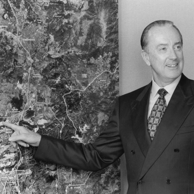 Black & white photo of Bob McLeod pointing to an aerial map