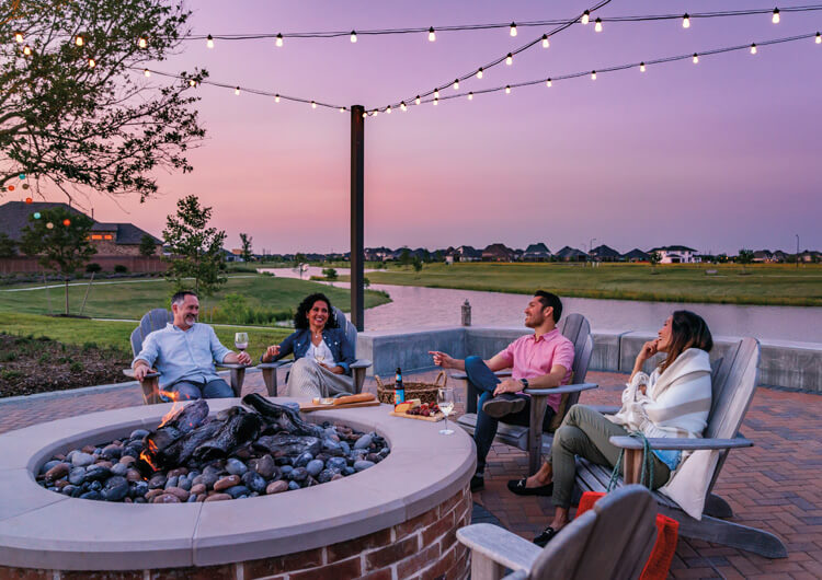 Four friends sitting by an outdoor firepit under string lights