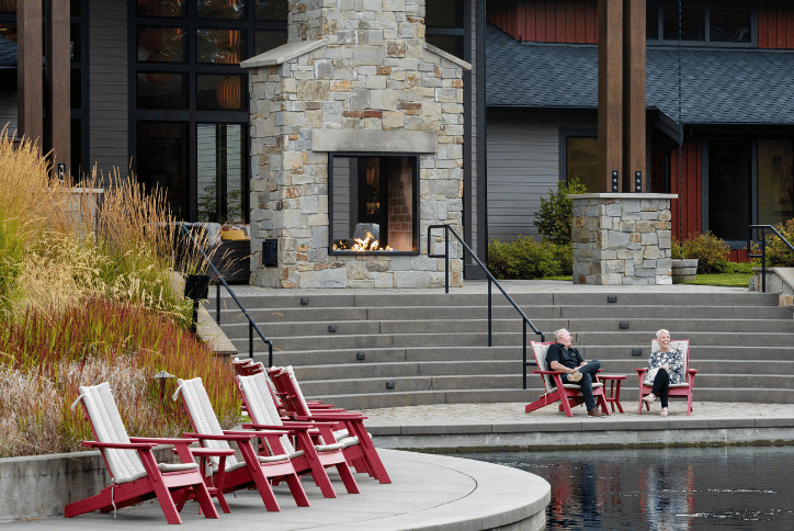 Senior couple sitting outside in red adirondack chairs near a water feature
